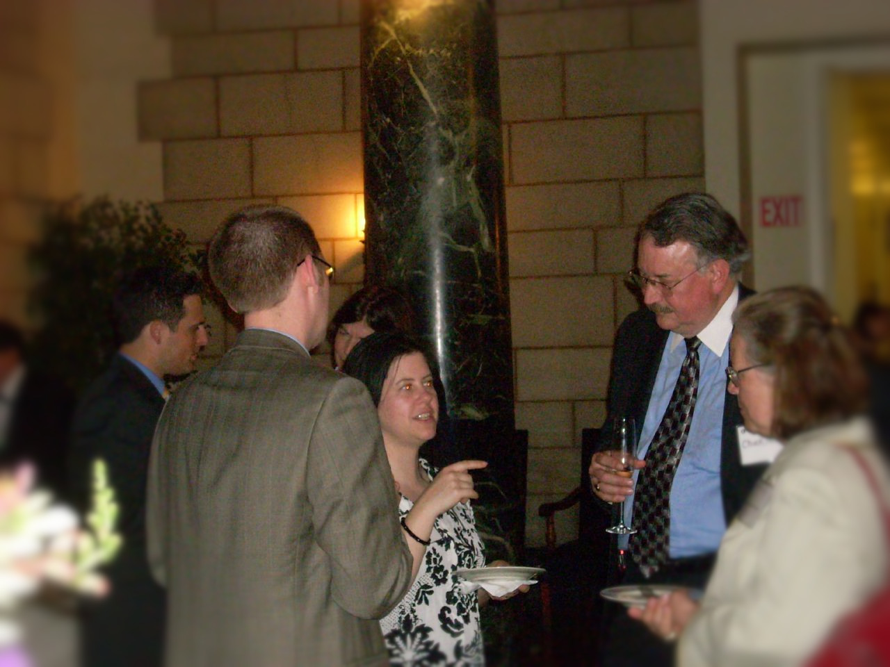 Two women and two men talk and gesture with plates and drink glasses during a business reception