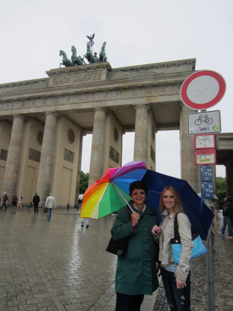 Nancy Gwinn holds a rainbow umbrella, standing with Grace Costantino in front of the Brandenburg Gate