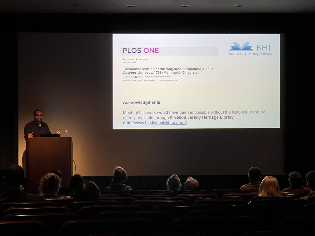 A man presents from a podium in a darkened auditorium