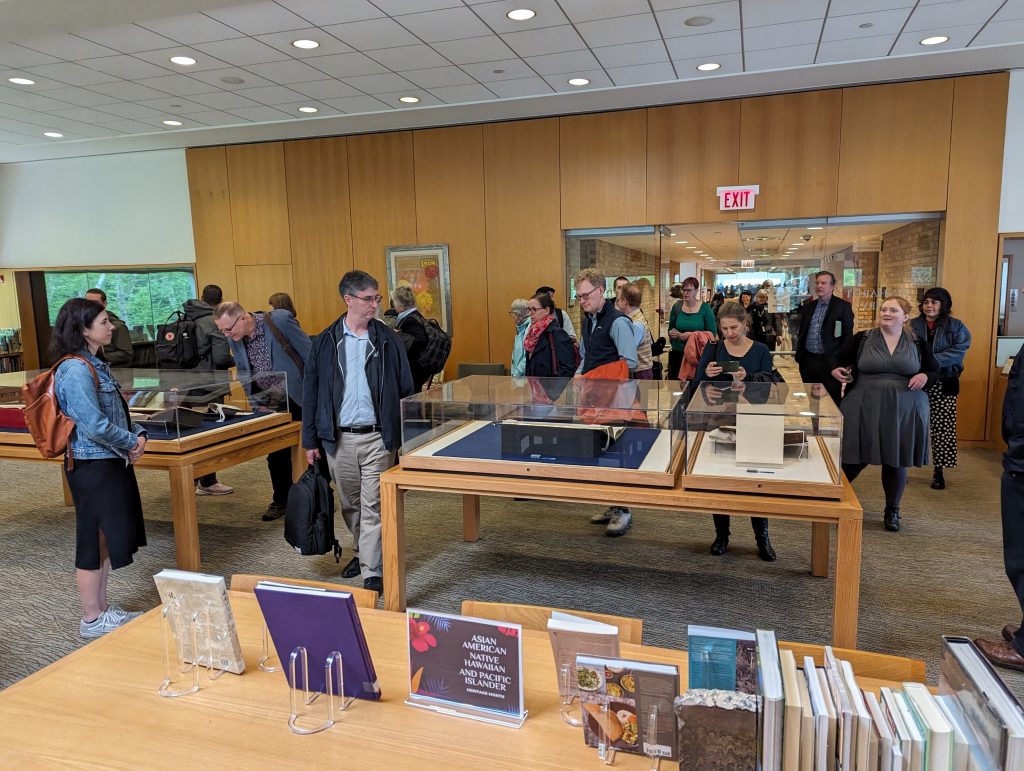 A crowd of people enter a library with rare books on display in glass enclosures