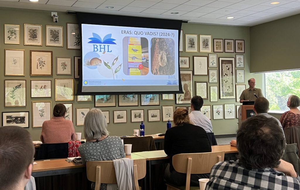 A man presents from a podium in a classroom full of botanical art