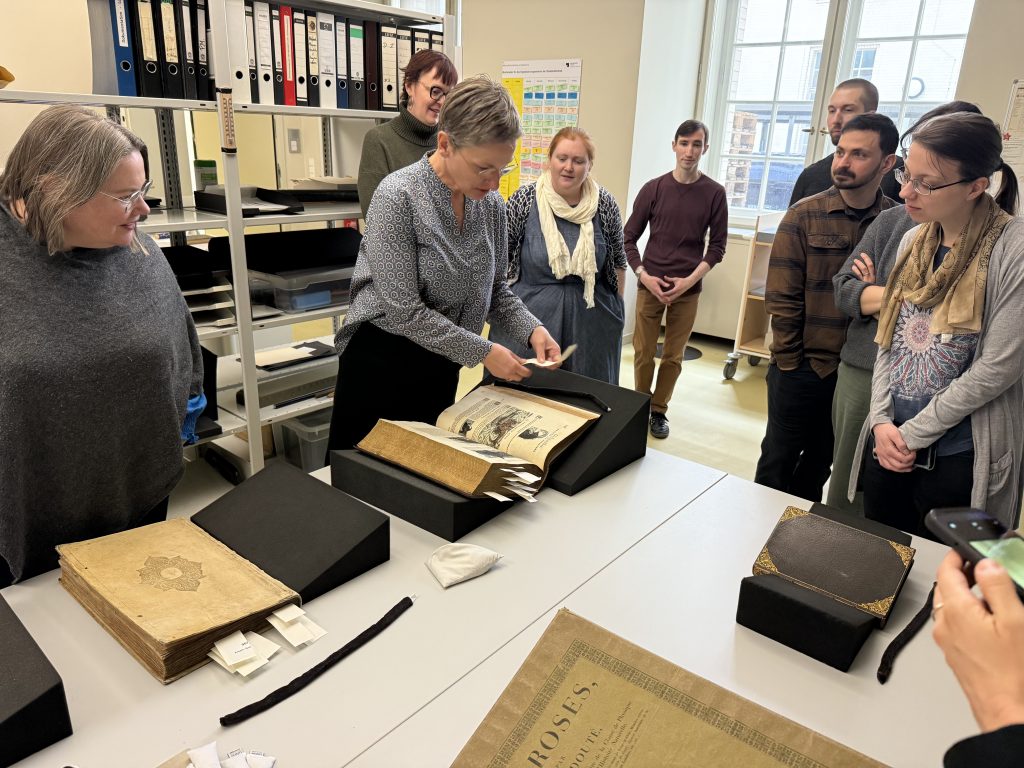 A group of people gather around a display table as a woman shares rare books nested in display cradles