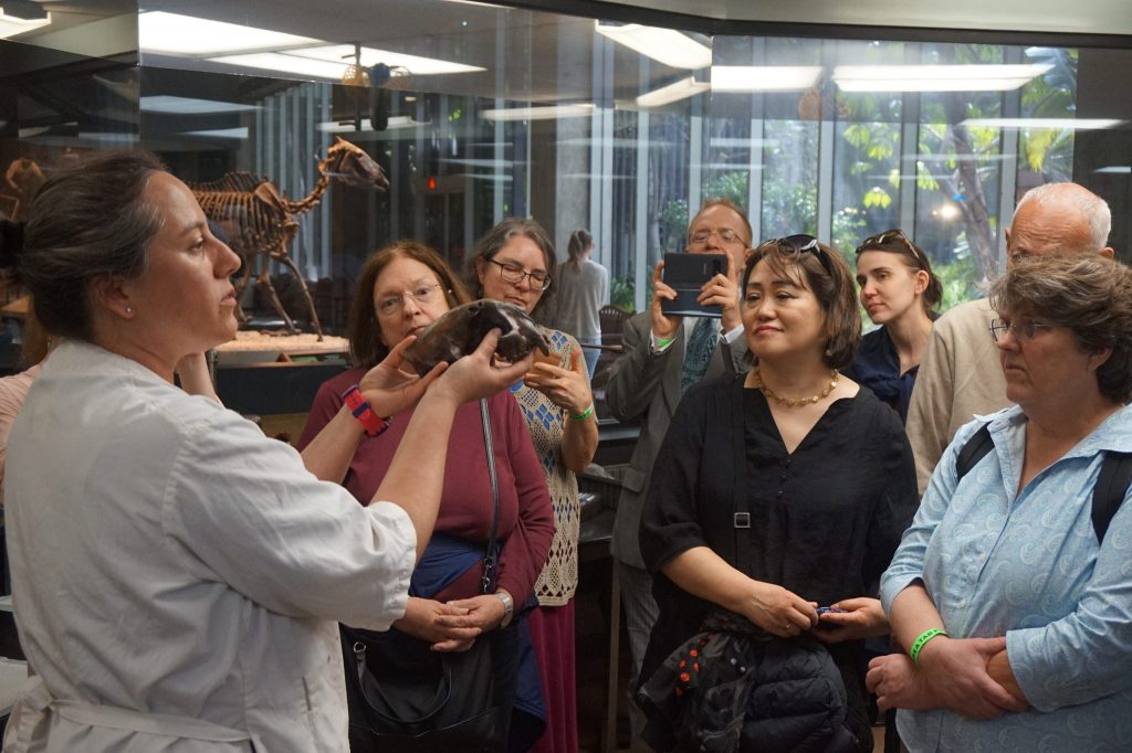 woman in white lab coat holding animal skull while group of men and women stand around her.