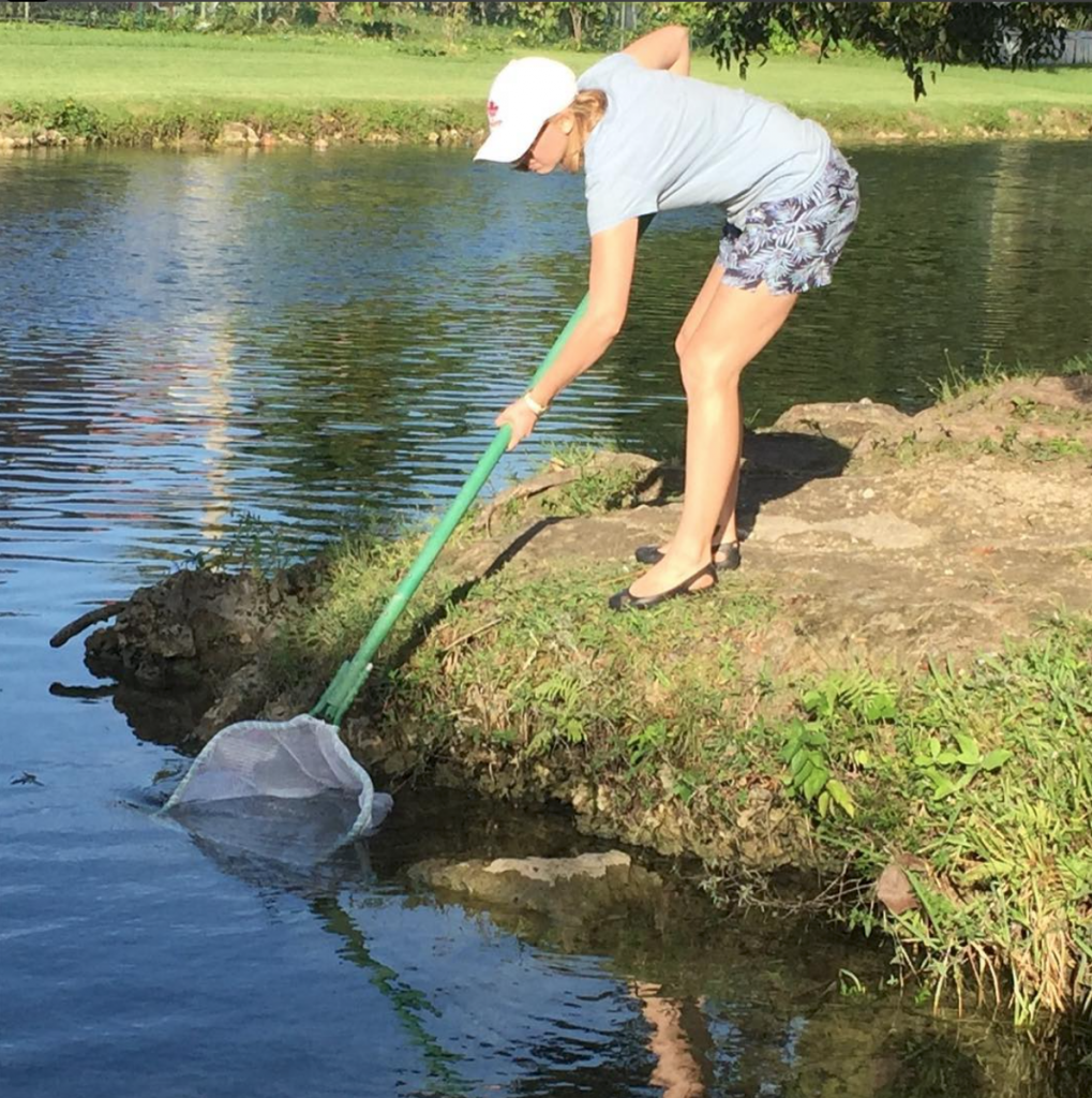 Blonde woman in shorts using a fishing net in a lake.