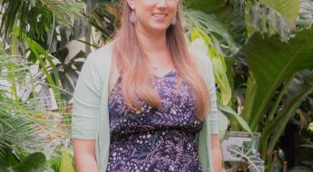 Photo of a woman standing in front of foliage.
