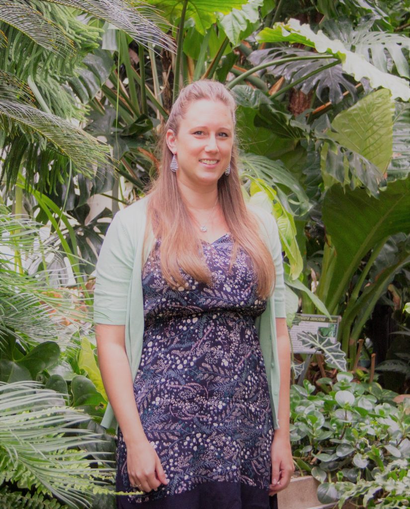 Photo of a woman standing in front of foliage.