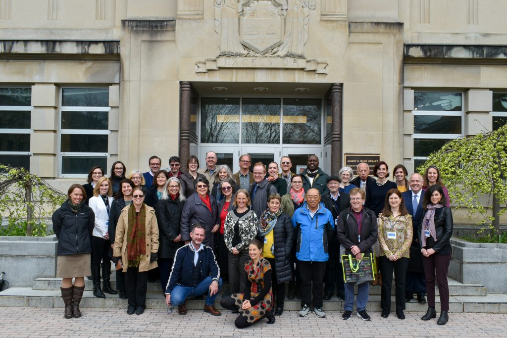 Group of men and women standing in front of doors at a stone building.