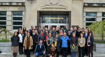 Group of men and women standing in front of doors at a stone building.
