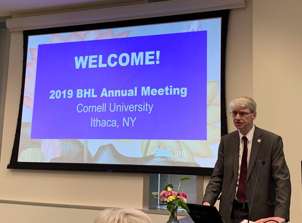 Man in suit standing in front of a slide that reads "Welcome! 2019 BHL Annual Meeting, Cornell University, Ithaca, NY"