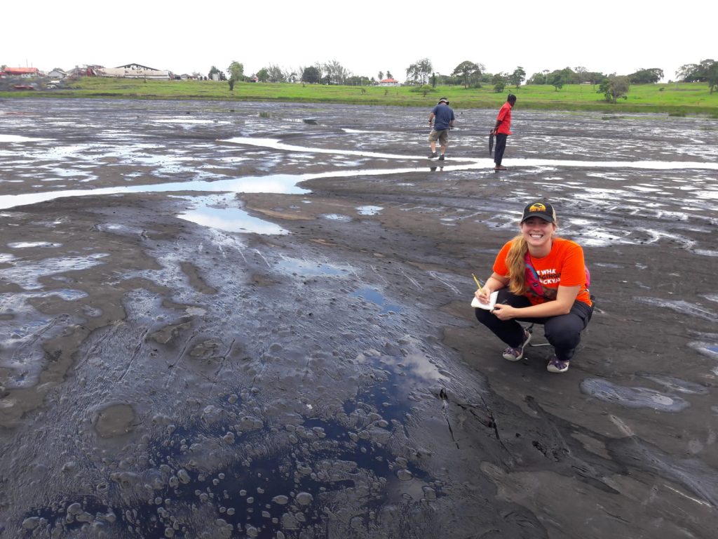 Photo of a woman kneeling by a tar pit.