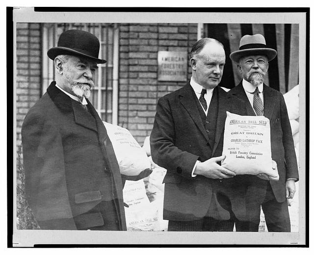 Black and white photograph of three men, one holding a sack of seeds with the text "American seeds to reforest France and Great Britain."