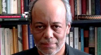 Photo of a man standing in front of a book case.