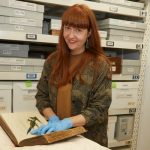 Photo of a person with red hair showing off a book in a storage room.