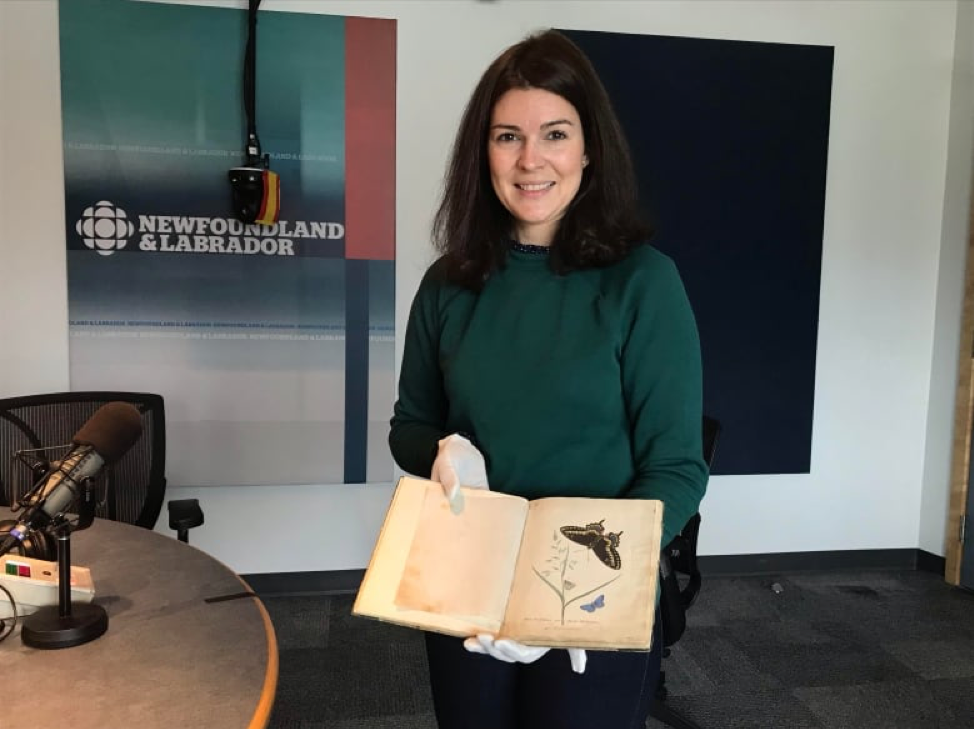 photo of a version with dark hair and green sweater holding a manuscript with illustrations of butterflies
