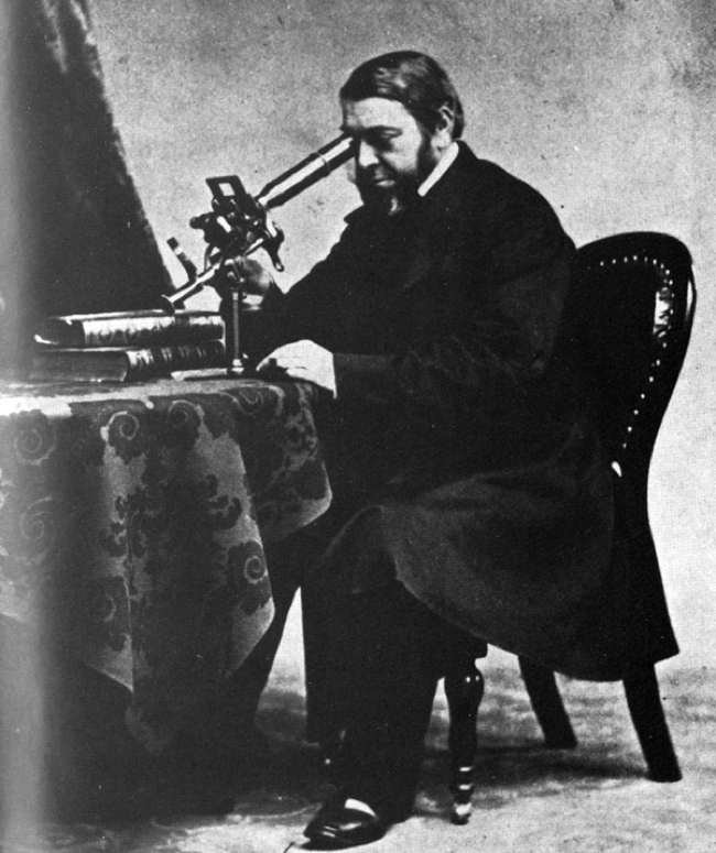 black and white photo of a man looking into a microscope