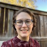 photograph of a human with glasses and brown hair standing in front of a fence outside.
