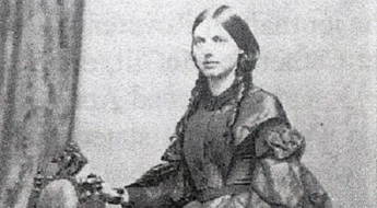 black and white photo of a person with brunette hair, braided, in 19th century dress.