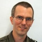 photo of a caucasian human with short dark hair and glasses