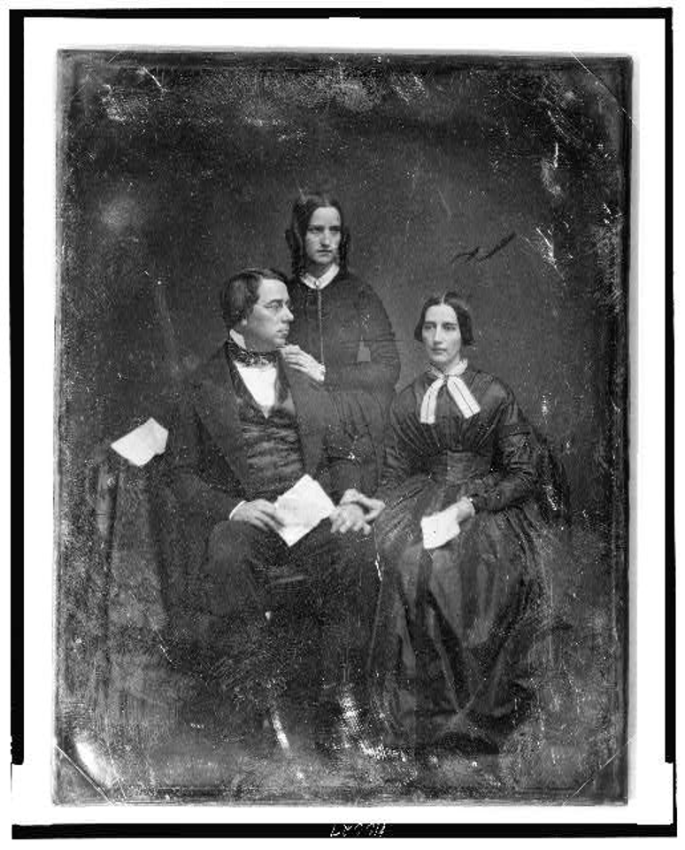 George Perkins Marsh family. Marsh seated beside a table with tablecloth, on the left, his head turned to the right, wearing spectacles, his wife seated on the right, her hand on his, her head slightly to the left, both holding papers; Caroline's sister, Lucy Crane, standing behind and between them, her hands on her brother-in-law's shoulder, her head three-quarters to the right] https://lccn.loc.gov/2004664023