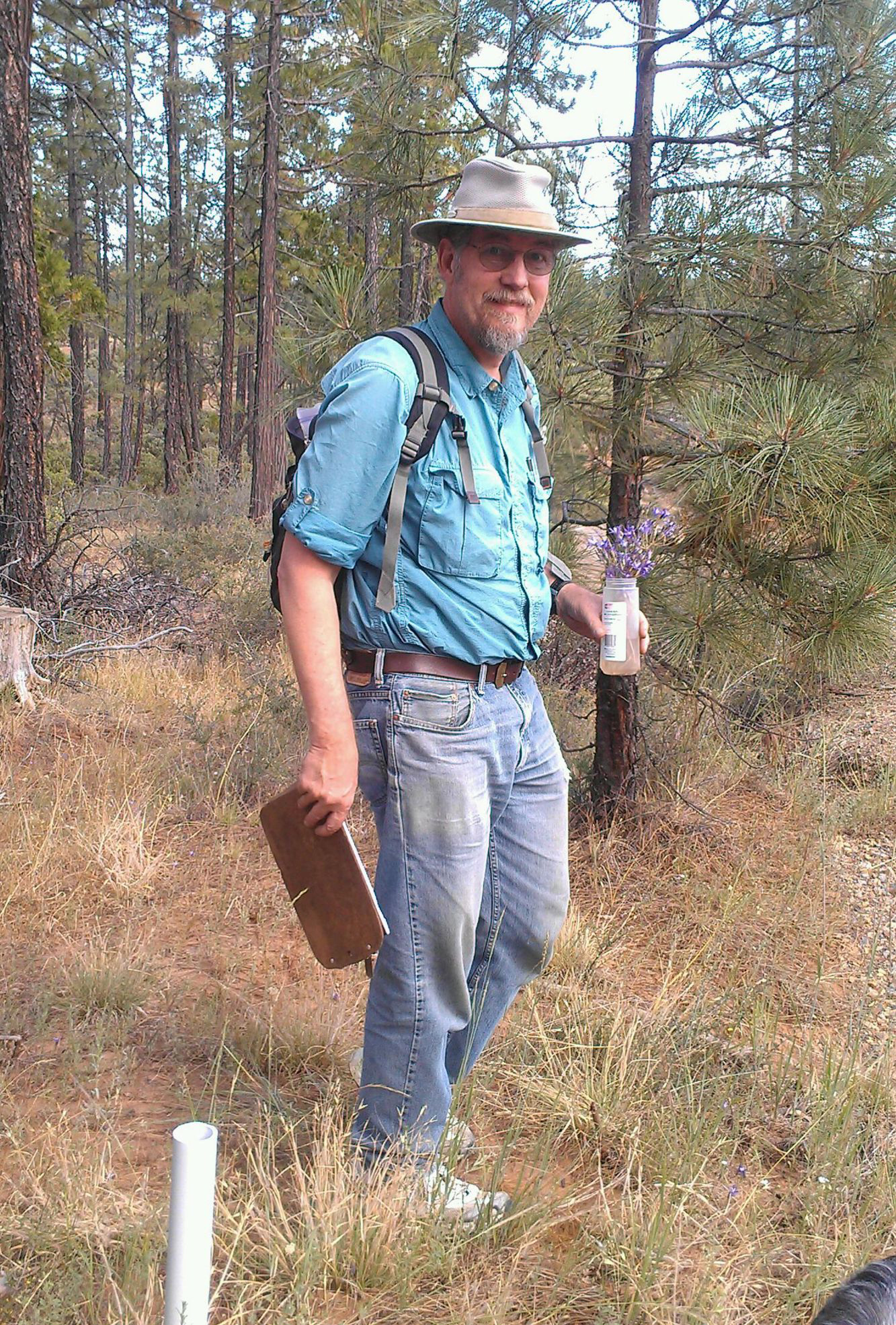 man in blue shirt, grey pants and khaki hat in a forest