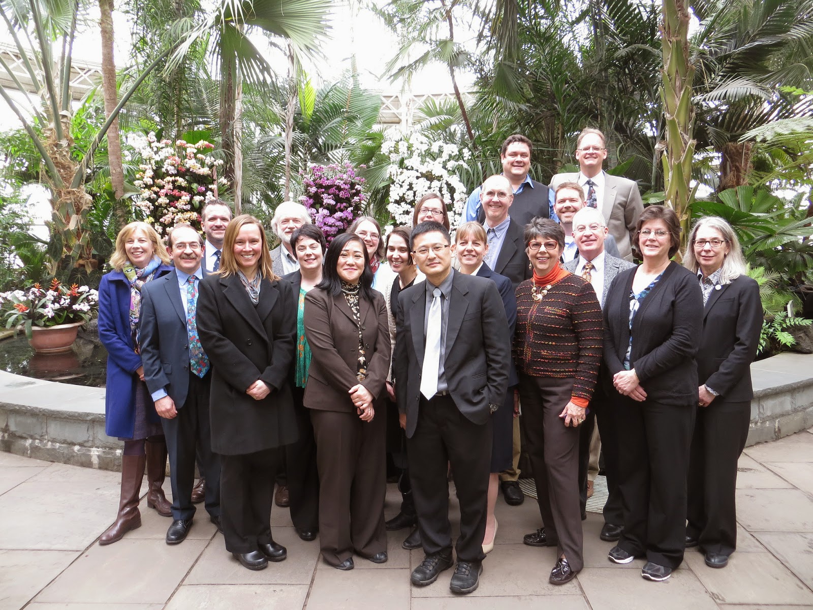 A group of people standing outside in front of a tropical garden of plants.