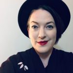 a person with fair skin in a black hat and black shirt with bright red lipstick.