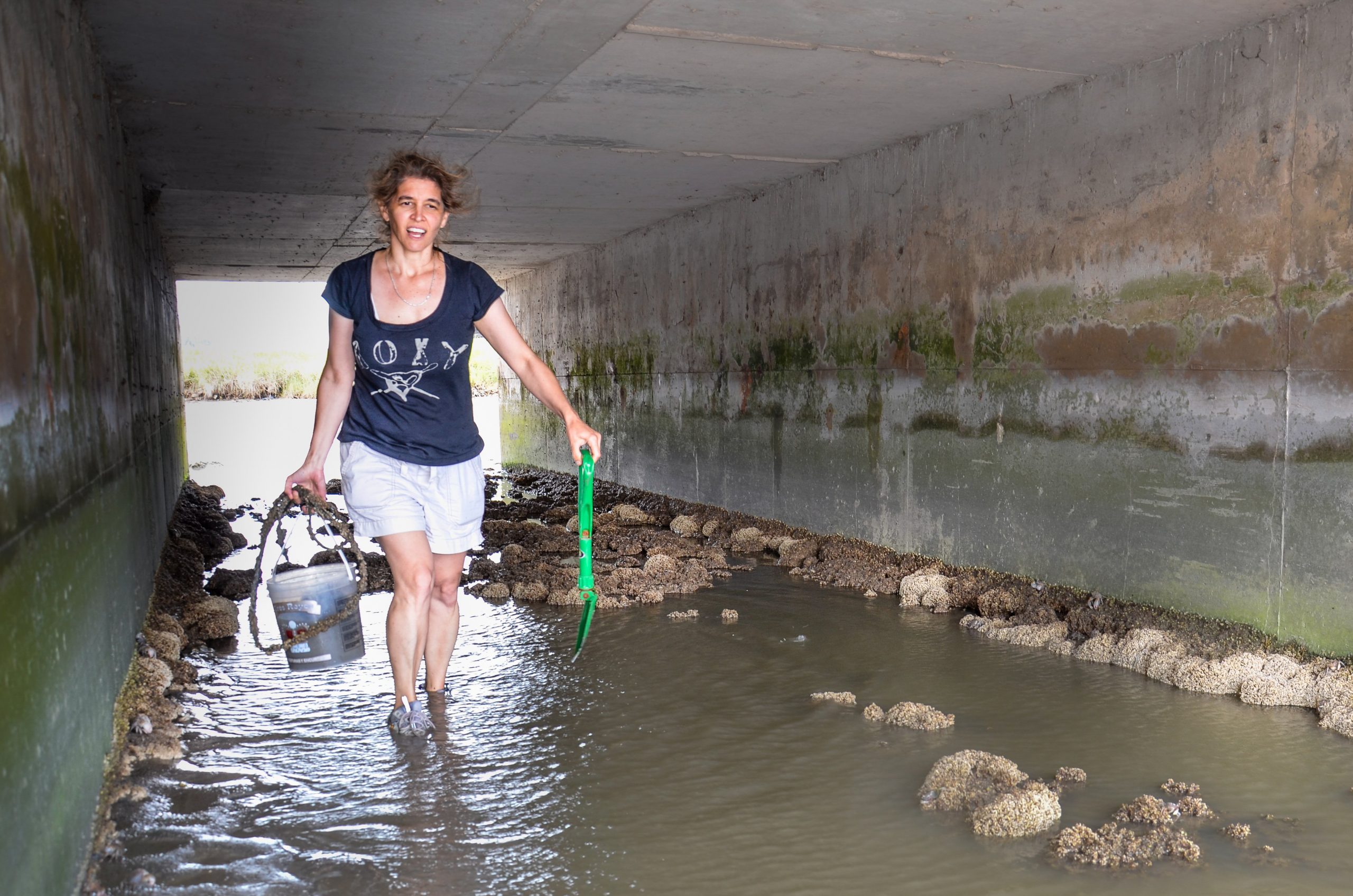 A woman in a blue shirt and white shorts walking through a tunnel with ankle high water.