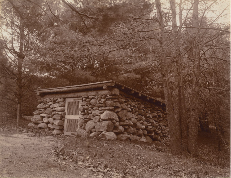 Black and white photograph of a stone wood-house in the woods.