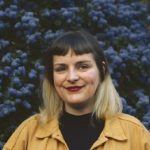A woman with short black hair, blonde tips, in a yellow shirt