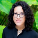 A woman with dark curly hair and glasses.