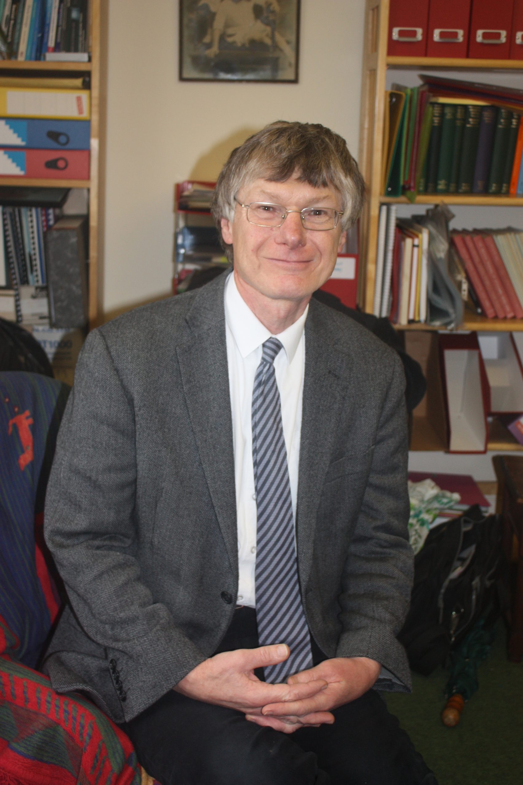 A man with white hair in a gray suit, white shirt, and blue tie.