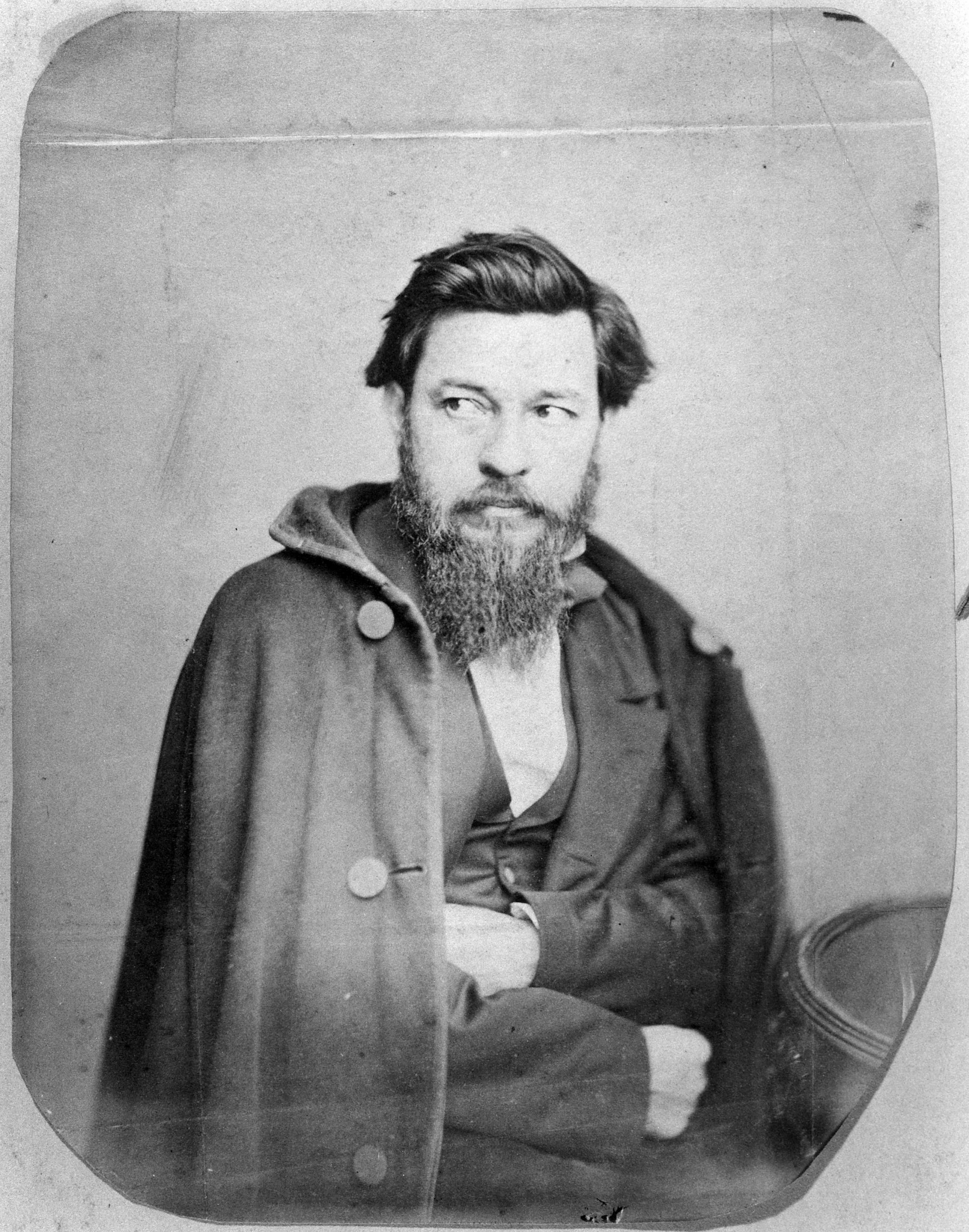 Black and white photograph of bearded man in overcoat, seated