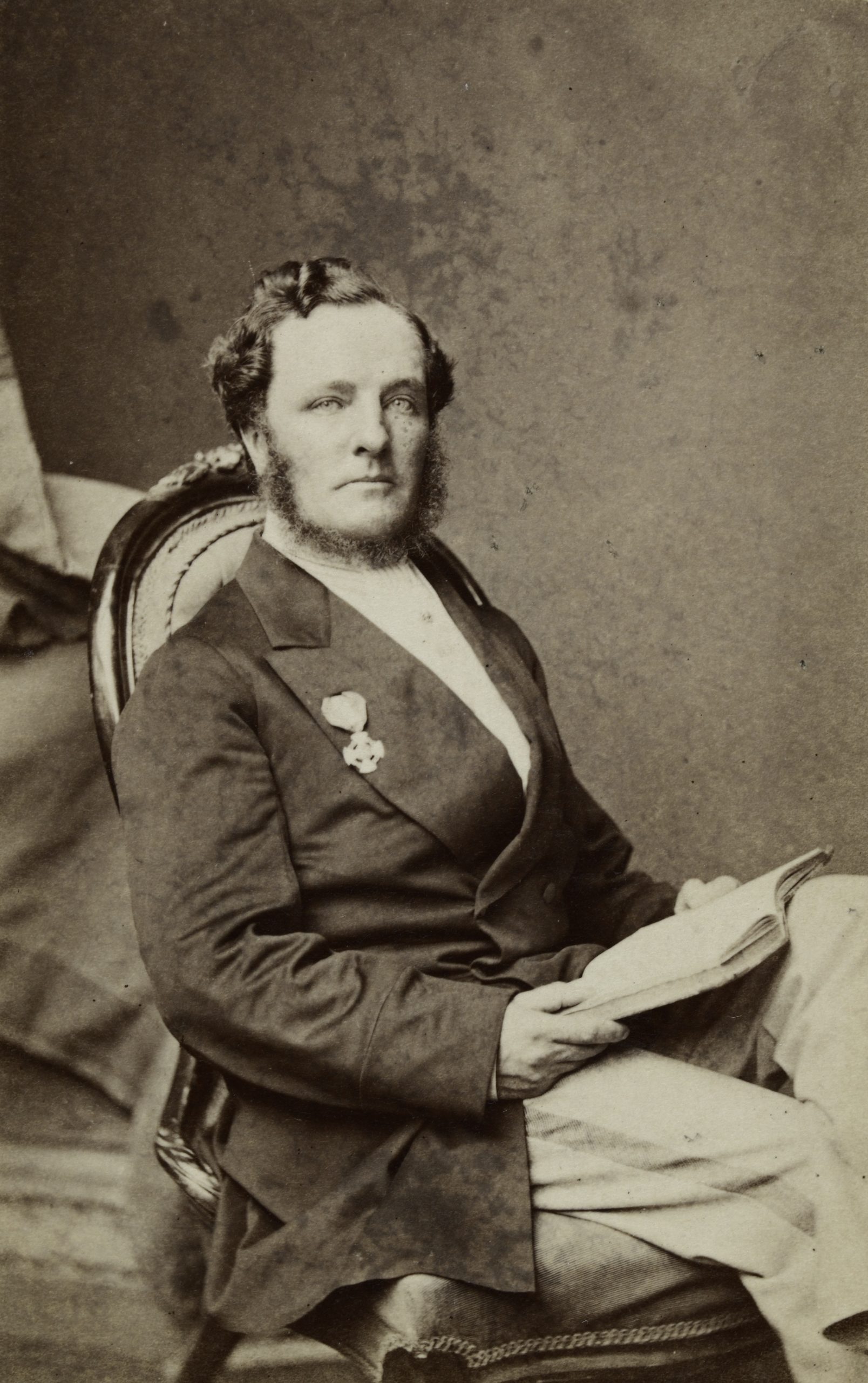 Portrait of a bearded man, seated with a book open in his lap