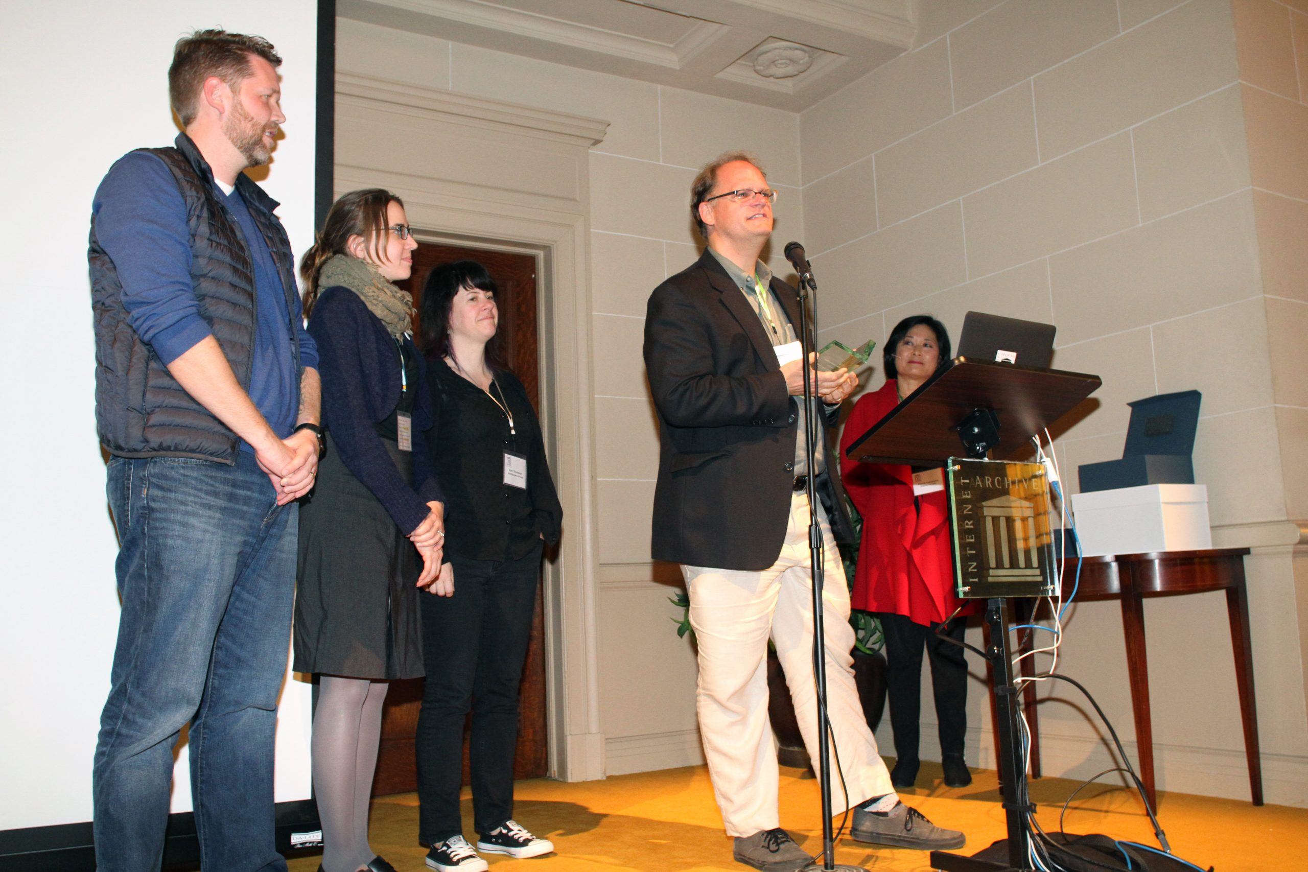 A man accepts an award at a podium while four colleagues look on
