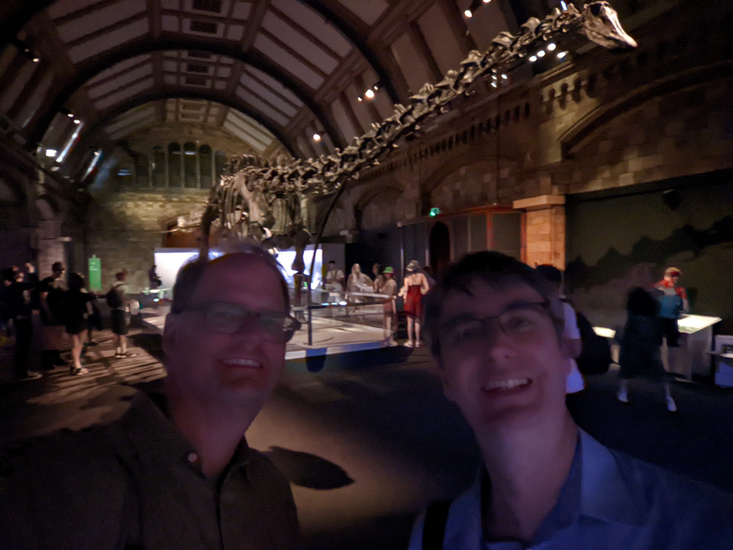 Two colleagues pose for a photo in front of an exhibit hall with a Diplodocus on display