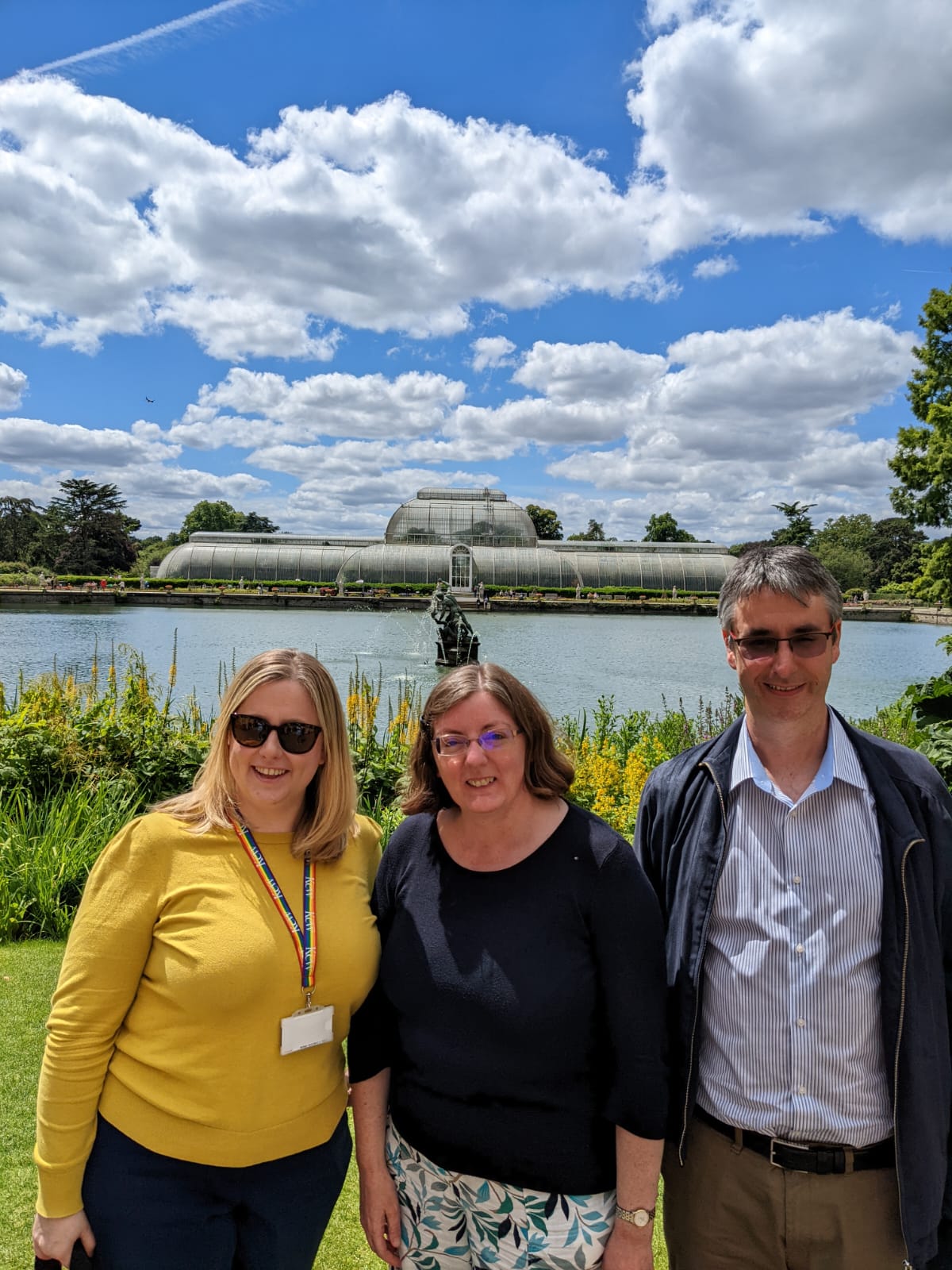 Three colleagues pose for a group photo in front of a water feature outside of the Royal Botanic Gardens, Kew