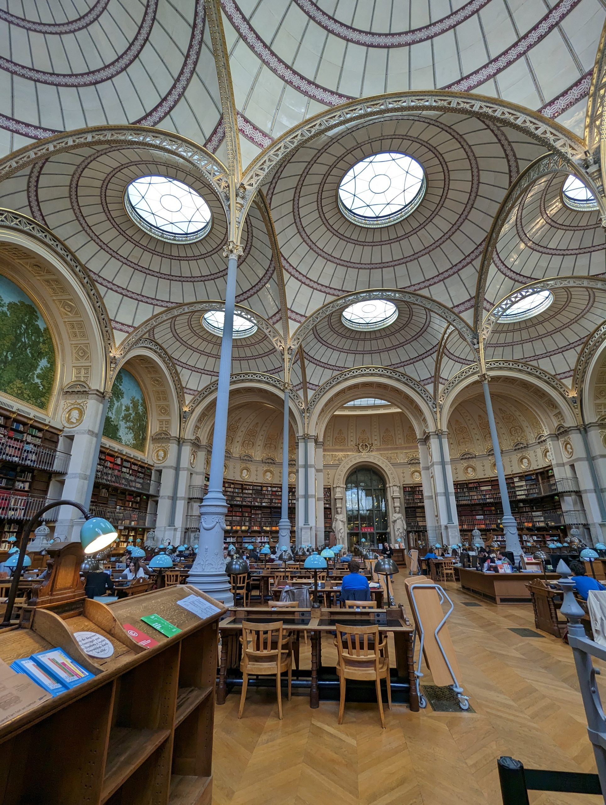 View of a BnF reading room with domed ceilings, ornate columns, and wooden tables and chairs