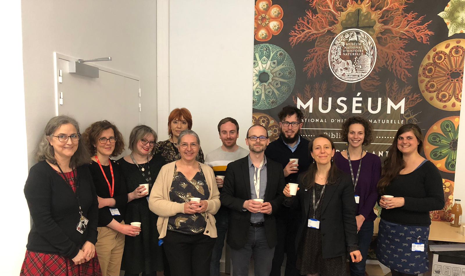The staff of MNHN libraries stand in front of the MNHN poster in the meeting room.