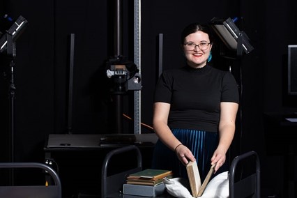 Woman with glasses holds open a book on a cart in preparation for digitization