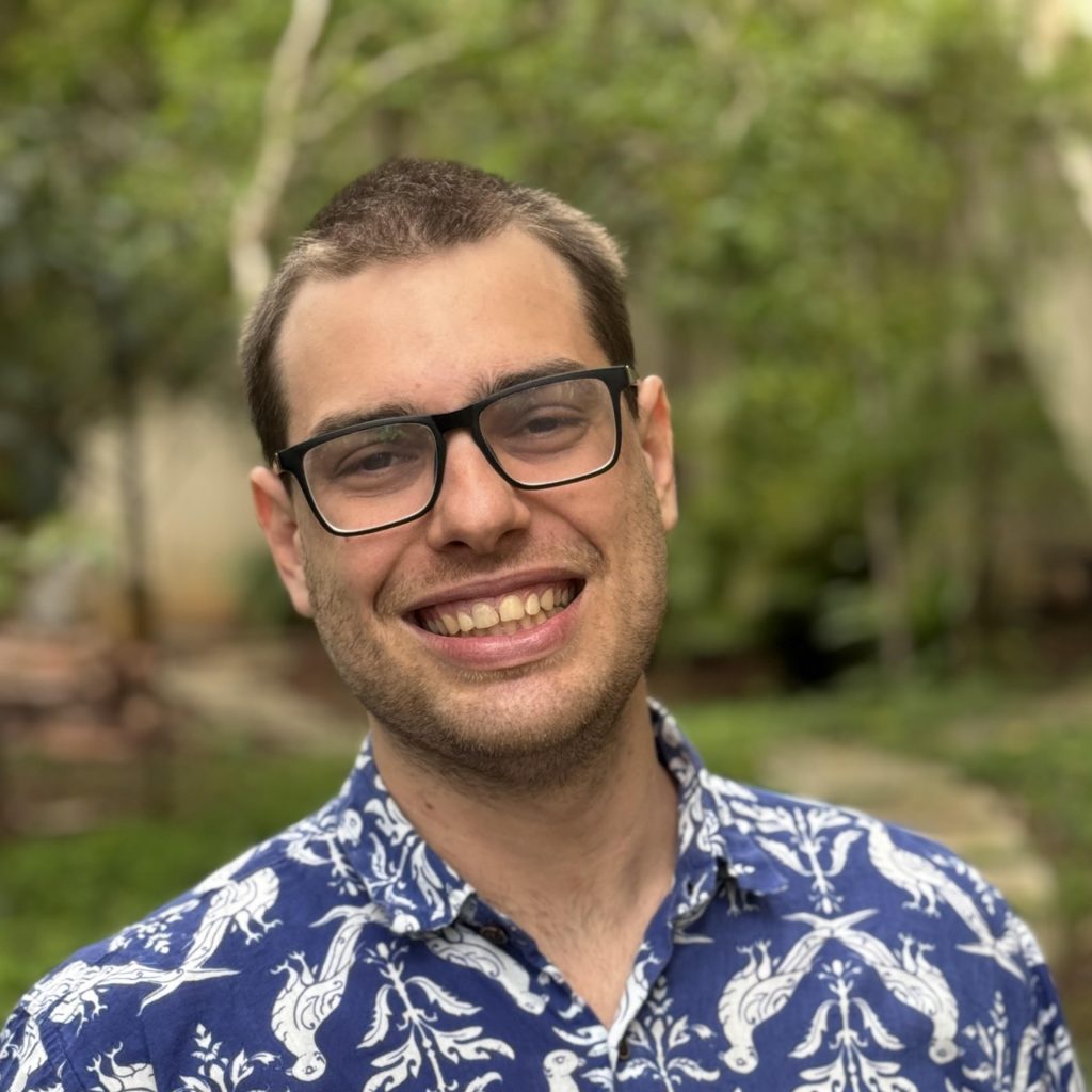 A person with short brown hair, black glasses, and a blue and white shirt smiles at the camera