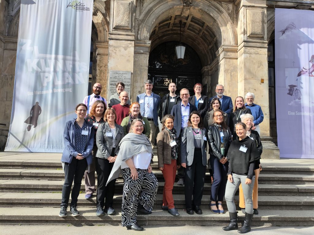 A group of people gather on the steps of the museum fur naturkunde berlin and smile for a photo