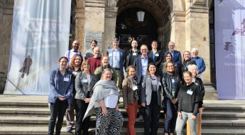 A group of people gather on the steps of the museum fur naturkunde berlin and smile for a photo