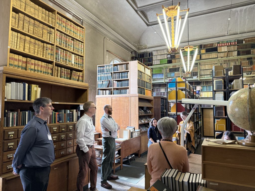 A group of people listen as a woman shares objects in a large library