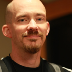 A man with a mustache and beard, wearing a dark shirt