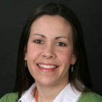 A woman with long brown hair, white collared shirt and green sweater