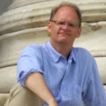 A man in a light blue collared shirt and glasses