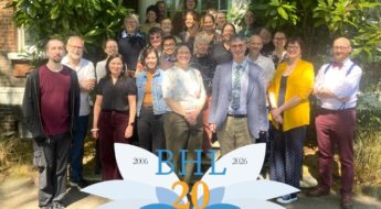 A group of 26 people posing for a group photo on the steps of a building in front of a green double door. The BHL at 20 logo is in the foreground.