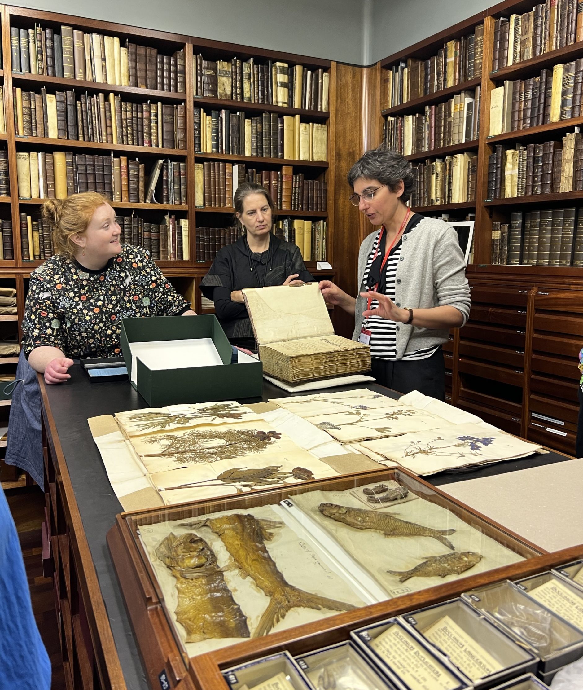 A group of people standing around a table covered in specimens and rare books in an archival storage room.