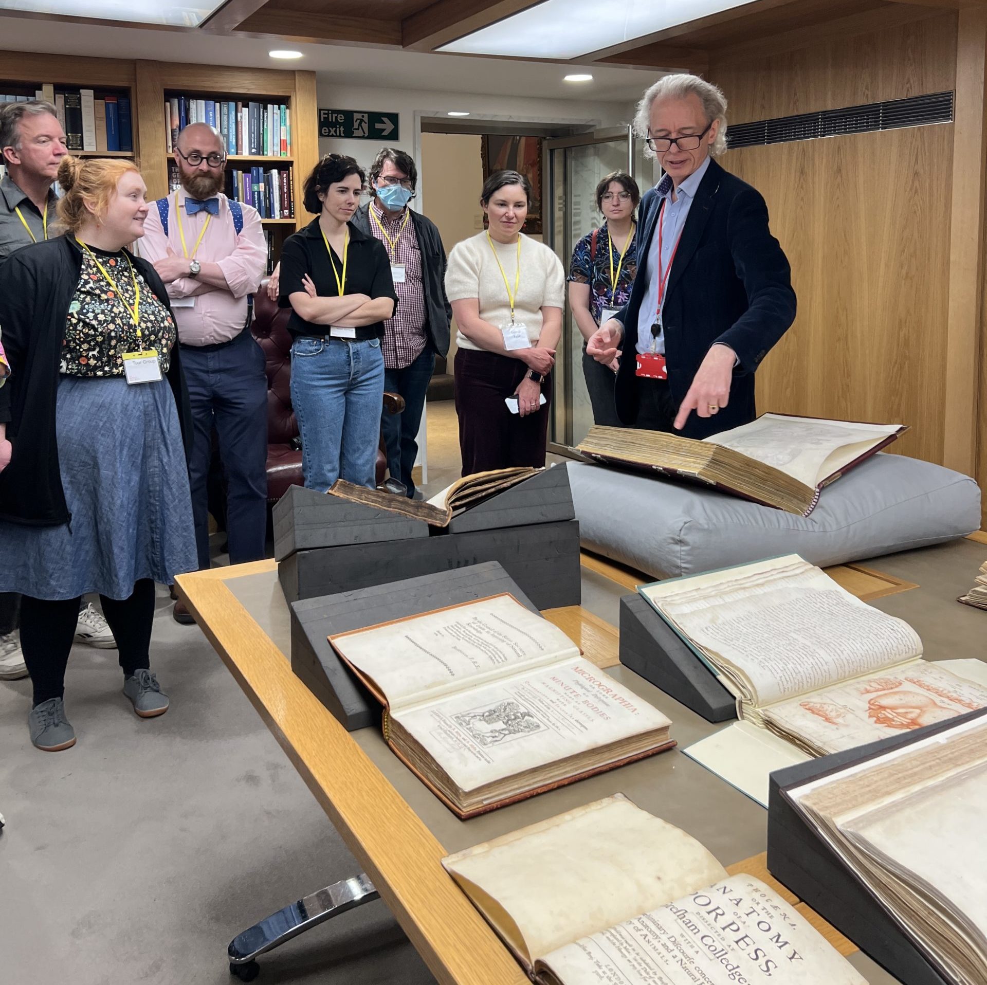 A group of people standing around a table with books on it. A man is pointing to one of the books.
