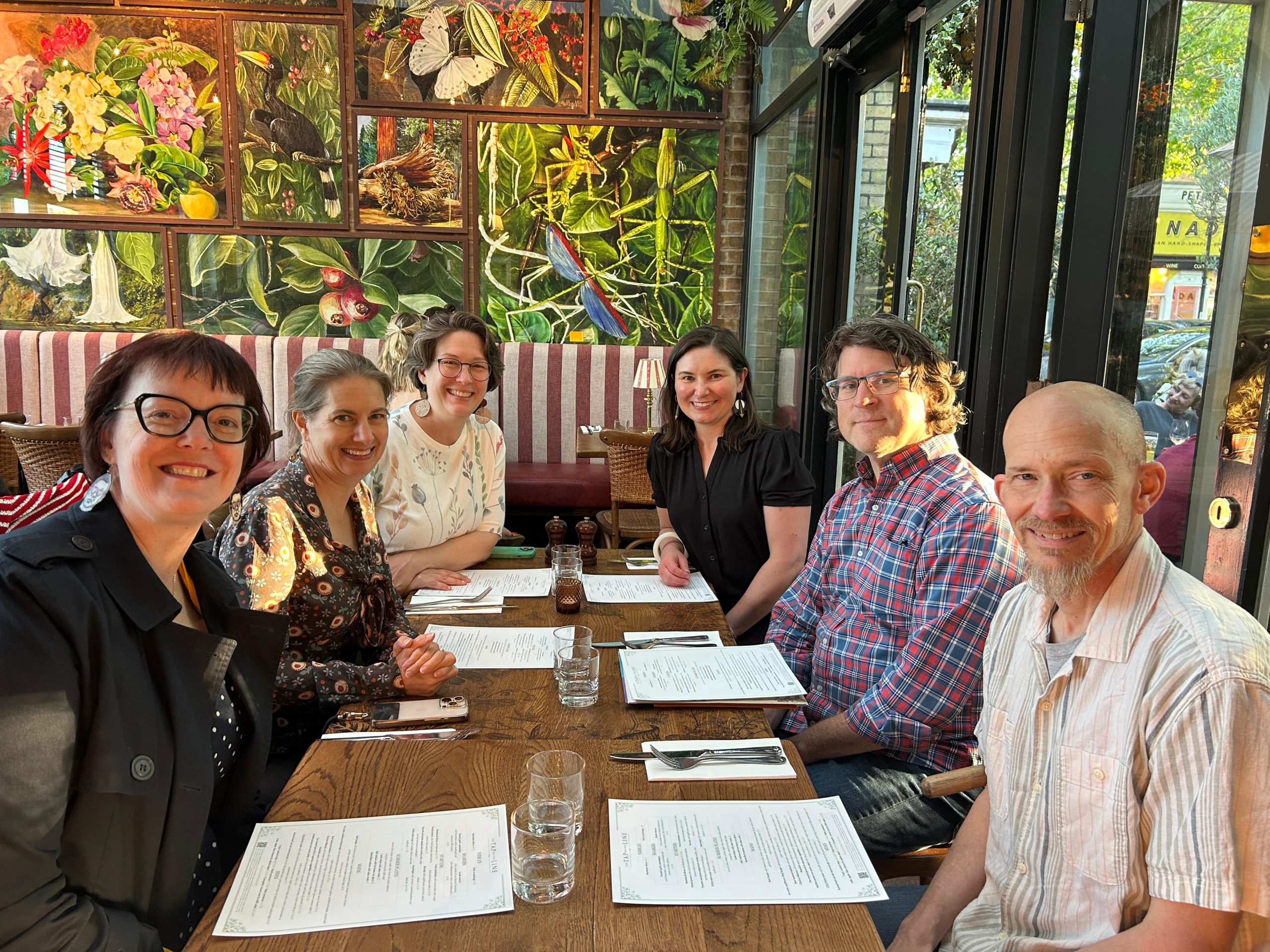 A group of six smiling people sitting around a table in a restaurant.